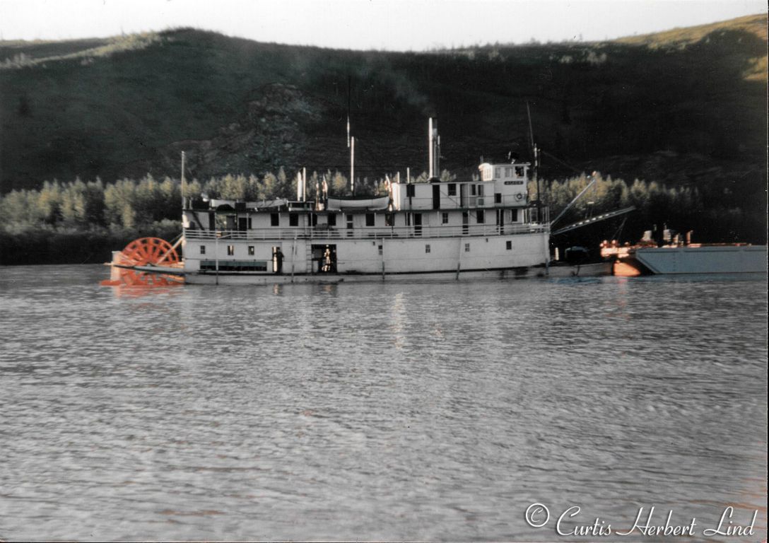 Another view of the Riverboat Alice with a fuel barge headed up the Tanana River above the town of Nenana. The ALICE was much smaller than the NENANA and you can tell the difference even at a distance by just counting the windows on the main deck. Also the proportion of the stern wheel to the hight of the deck on the Alice is smaller.