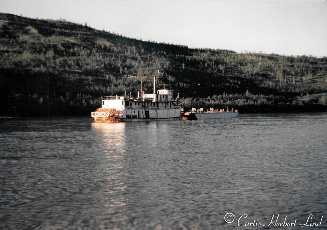 River Boat Nenana underway up river from Nenana with a fuel barge. There were several communities such as Galena and McGrath that had military airfields built in anticipation of WWII that were supported by regular deliveries by the River Boats operated by the Alaska Railroad. Notice the native cemetery on the hill in the background.